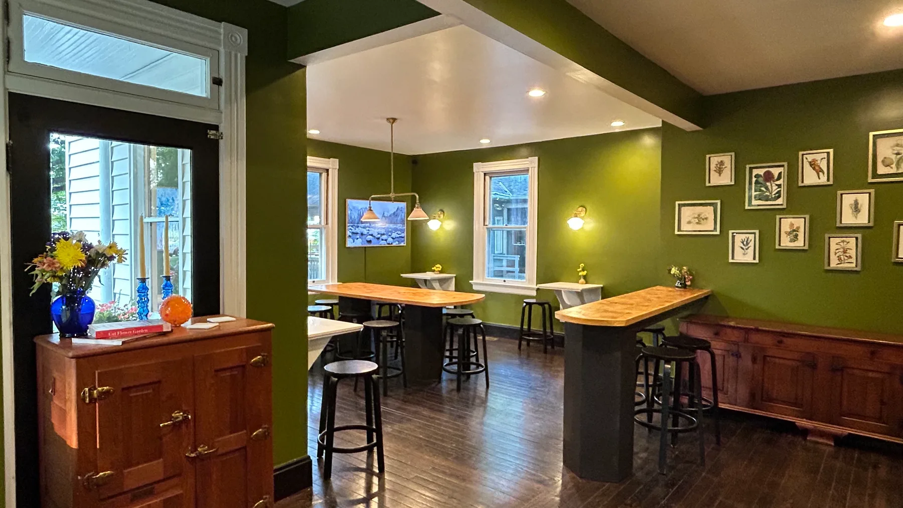 Inside the Farmhouse: green walls, wood bar tops with stools, and framed botanical prints